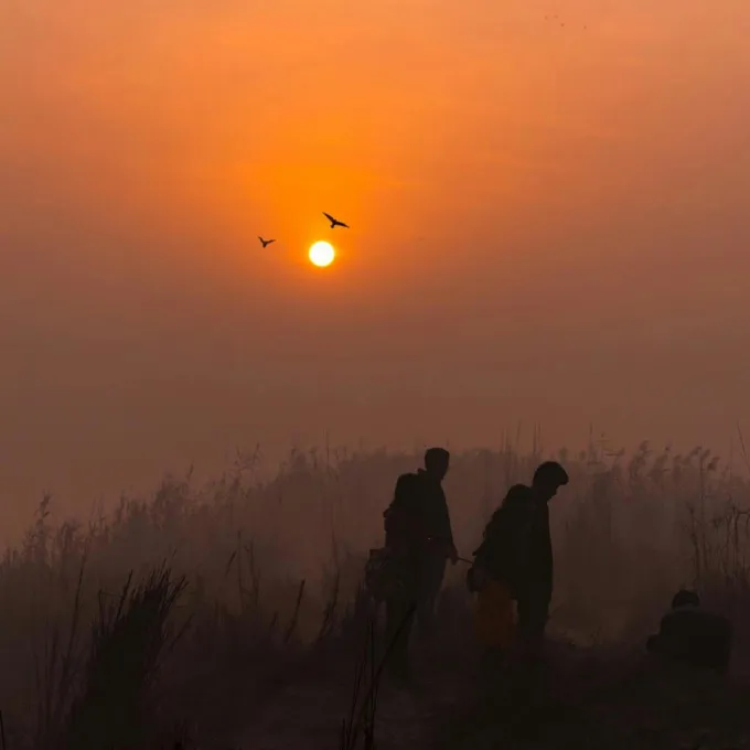 "two people walking across a hilly landscape at sunset"