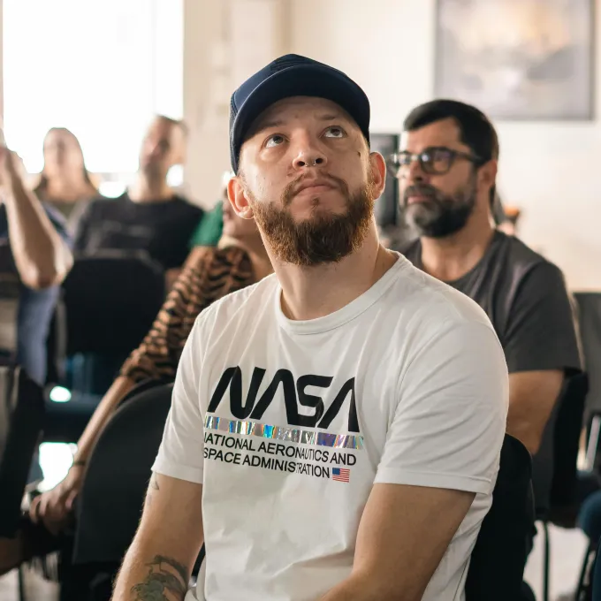 "man in a NASA shirt sitting in a public forum"