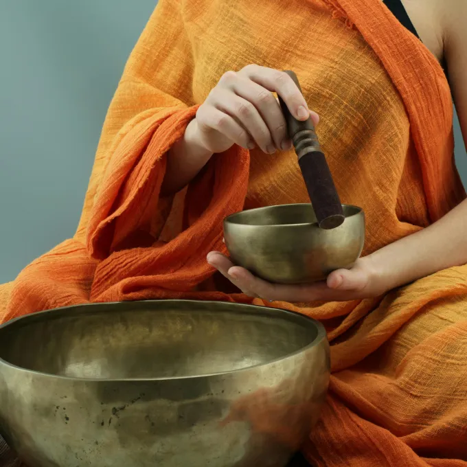 "a person in orange robes using sound bowls to meditate"