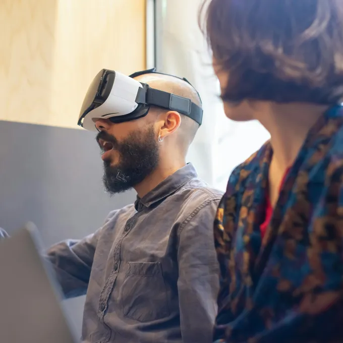 "a man wearing a VR headset and talking to another person"